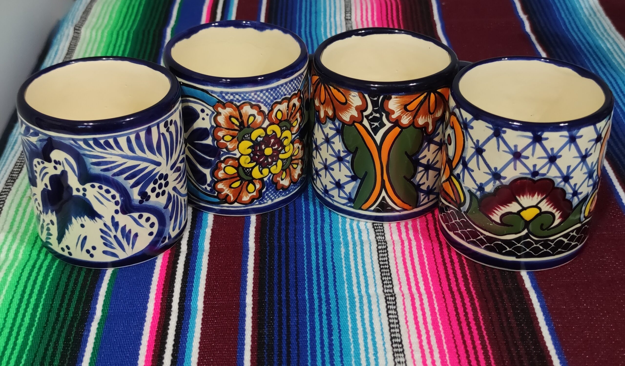 Four hand-painted Talavera-style mugs from Dolores Hidalgo on a striped Mexican blanket
